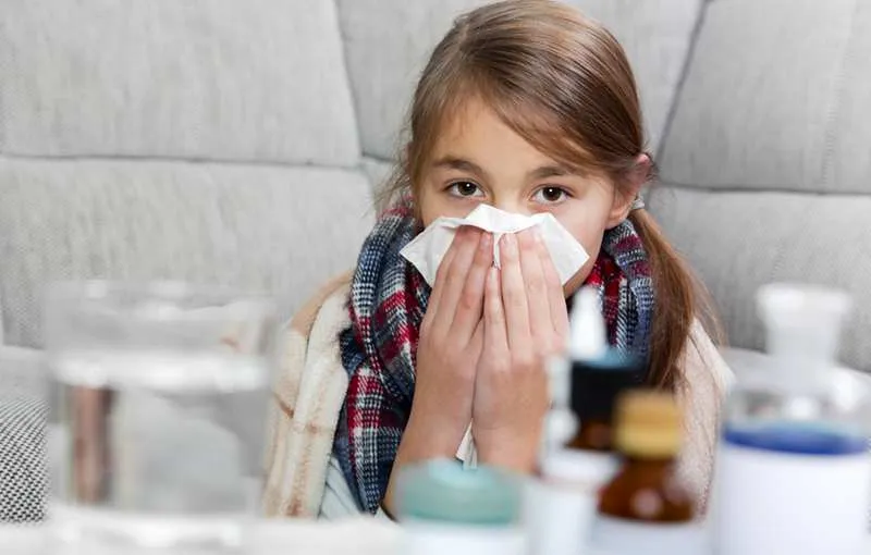 Young girl sneezing into a facial tissue while cleaning her nose