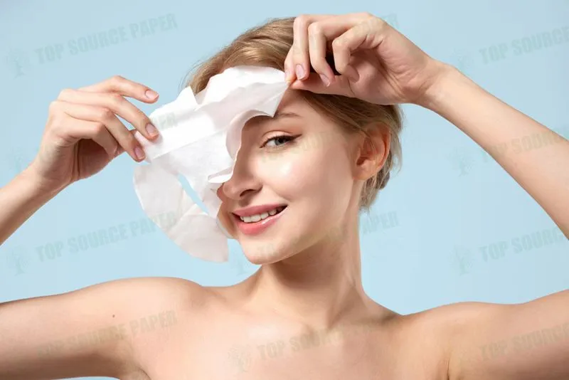 A young woman removing a hydrating sheet mask from her face while smiling