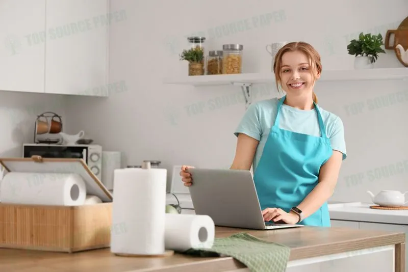 A young woman is at a table using a laptop surrounded by paper napkins.