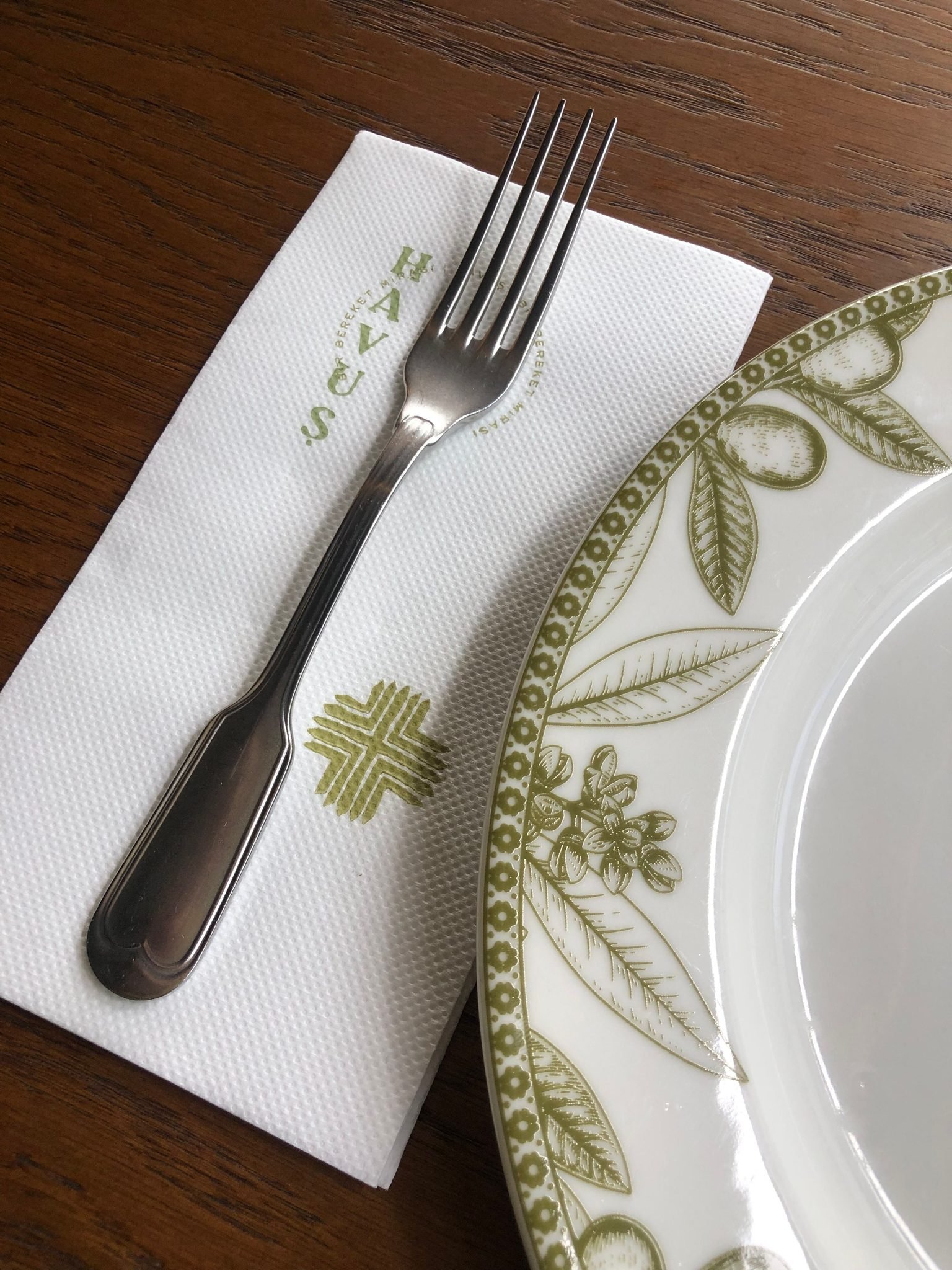 Custom logo-printed white paper napkin laid on a wooden table with a steel fork